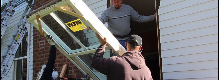 The homeowners wanted replace their single-pane, two-over-two windows with ‘true’ wood windows. Here, carpenters James Curtis (center), Ed Brady (right), and Isaias Santos (left), work from the exterior; lifting a full-frame Marvin Ultimate double hung window in place.