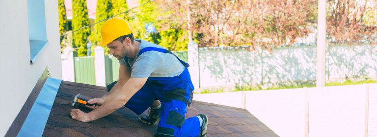 Professional roofer in uniform and safety helmet with a hammer in hand is fixing the roof on the new house