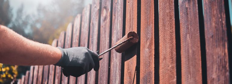 Process of fence renovation at bright sunny day by man in protective gloves.